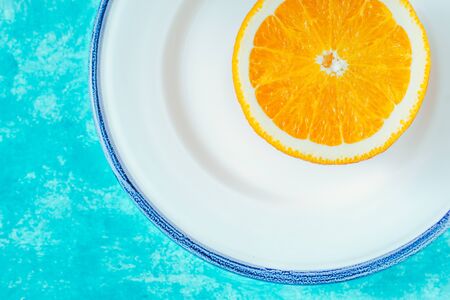 Half of orange on the white plate on the cyan background horizontalの写真素材