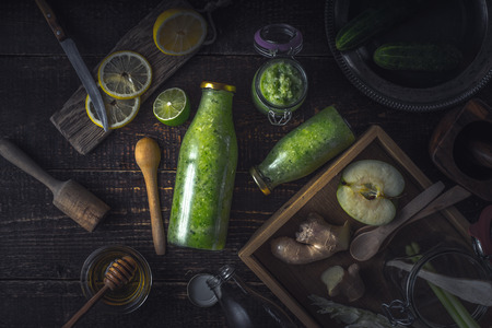 Bottles  and jar with  green smoothie and different ingredients on the wooden tray horizontalの写真素材
