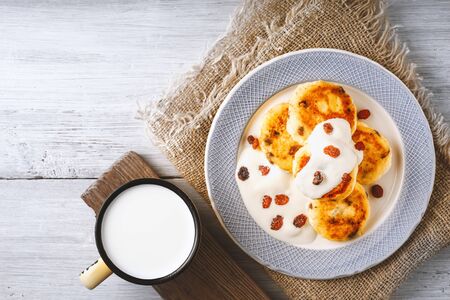 Cheese pancakes with raisins and yogurt on a ceramic plate on the wooden tableの写真素材
