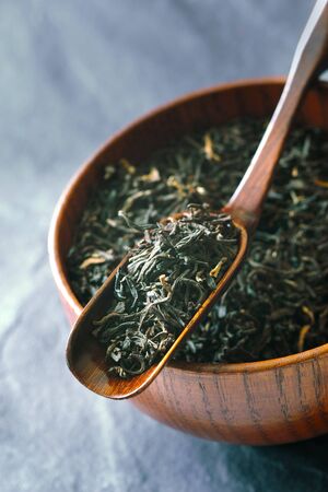 Tea leaves on the wooden bowl  with spoon on the   stone background verticalの写真素材