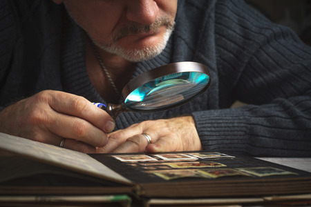 Man considers album of postage stamps trough the magnifying glass horizontalの写真素材