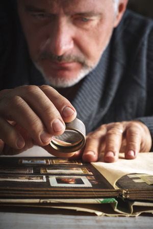 Man considers album of postage stamps trough the magnifying glass verticalの写真素材