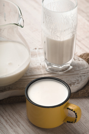 Glass and pitcher of kefir and cup on a white stand verticalの写真素材