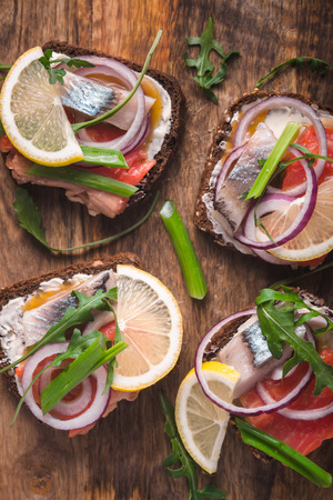Sliced bread with smoked salmon, herring, lemon and arugula verticalの写真素材