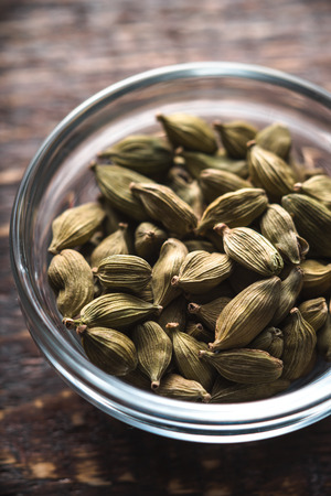 Cardamom seeds in a bowl on a brown board verticalの写真素材
