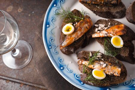 Sardines, quail egg on rye bread on a ceramic plate and glass horizontalの写真素材
