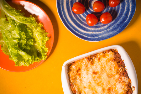 Lasagna, tomatoes, green salad on a yellow backgroundの写真素材