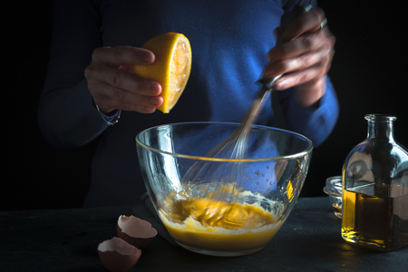 Lemon is squeezed into a bowl with yolks and mustard close-upの写真素材