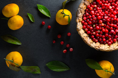 Yellow mandarins with leaves and cranberries in a basket on a gray stone free spaceの写真素材