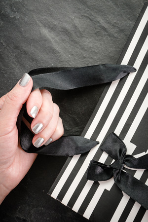 Female hand holding a package in white and black stripes with a bow close-upの写真素材