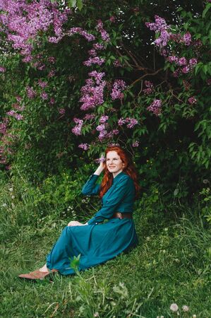 Red-haired girl with freckles standing near a lilac bushの写真素材