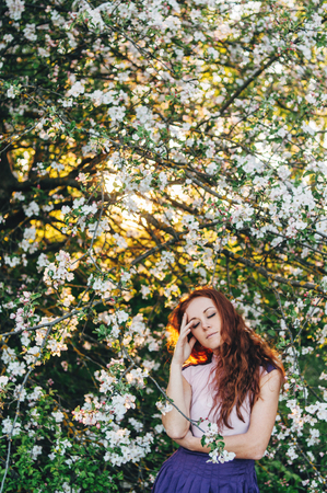 Red-haired girl with freckles near apple tree in white dressの写真素材