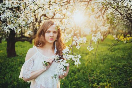 Girl in a white dress among a blossoming apple tree