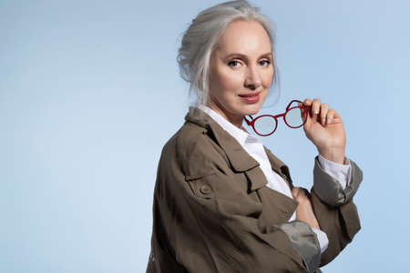 Beautiful stylish senior woman holding eyeglasses. Studio portrait of confident elderly lady editor....
