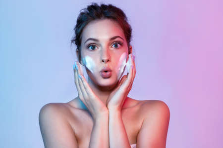 Young woman washing face with cleansing skin foam and looking at camera with surprising.の写真素材