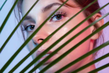 Close-up of woman looking through tropical leavesの写真素材