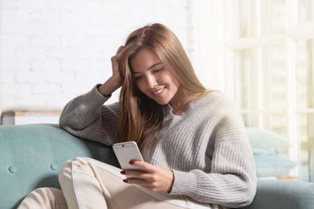Young woman sitting with smartphone on sofa at home and resting