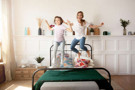 Mother and daughter spend their free time together, having fun at home and jump on the bed
