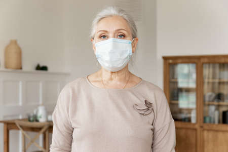 Pretty senior female in medical protective mask from coronavirus pandemic spread. Elderly woman...