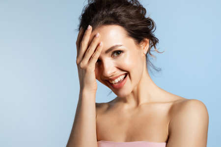Beautiful laughing woman with pure skin. Cute smiling young girl with beauty face feeling little bit shy, surprise, shock or pleasure isolated studio headshot on blue.の写真素材