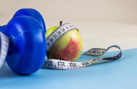 Blue dumbbells, measuring tape and apple on a blue background. Healthy lifestyle, the concept of body weight loss. Cares about the body. Empty place for text.の写真素材