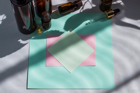 Dark cosmetic bottles and green natural leaves on a light background. Green empty card, sheet for...