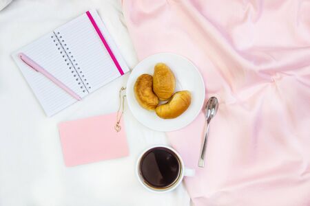 Breakfast in bed. Flat composition with coffee, croissants and a notebook for writing. Lifestyle concept frame. Top view on sheetsの写真素材