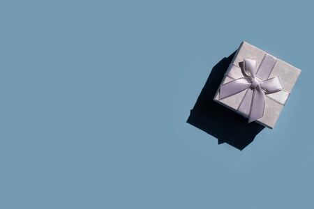 White gift box with hard shadows and bright lights on a blue background with space for writing....