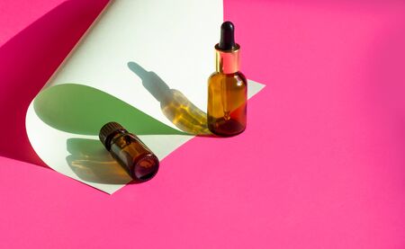 Glass cosmetic bottles on a bright pink background with hard shadows. Beauty blogger, procedures salon concept. Minimalism. Cosmetic dropper on a pink background.の写真素材