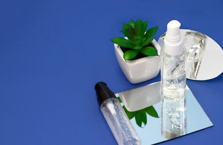 Cosmetic bottles with serum, face cream on a bright blue background with mirrors. Beauty blogger,...