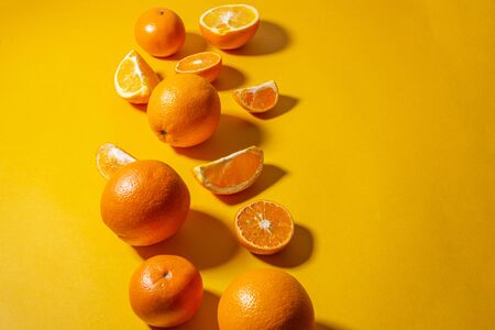 Oranges and tangerines whole and cut into pieces on a bright yellow background. minimalist concept.
