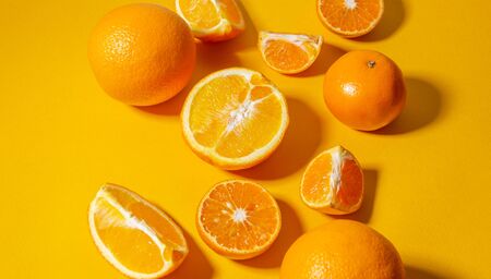Oranges and tangerines whole and cut into pieces on a bright yellow background. Minimalistic backgroundの写真素材