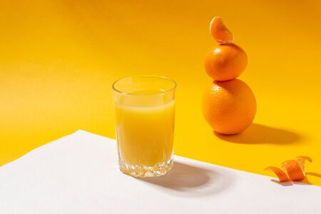 A glass of orange juice, orange and mandarin on a bright yellow background. Freshly squeezed orange juice. Copy space, minimalist conceptの写真素材
