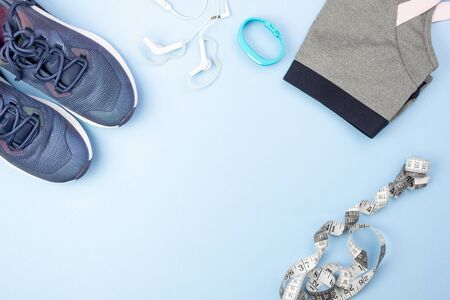 Sports flat layout. Fitness accessories sneakers, clothes, earphones and watches on a blue background. Doing sports and fitness at homeの写真素材