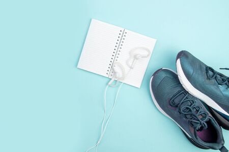 Sports flat layout. Fitness accessories sneakers, headphones and an open notebook for recording on a blue background. Sports Planning.の写真素材