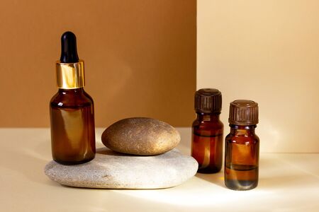 A glass cosmetic bottle with a dropper stands on a stone on a beige background with bright sunlight. Natural cosmetics concept, natural essential oil.の写真素材