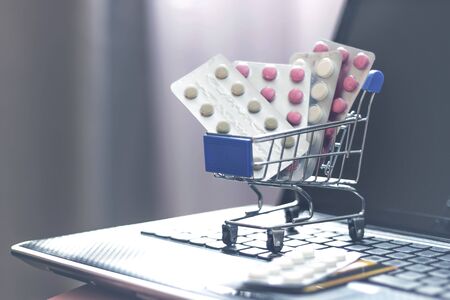 Shopping basket with pills and drugs and a credit card on a laptop keyboard. Buying medicines online, buying pills from home.の写真素材