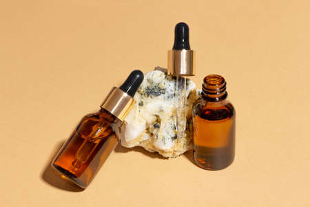 Natural cosmetics in glass bottles with a dropper stand next to a stone on a beige background with bright sunlight. The concept of natural cosmetics, natural essential oil.の写真素材