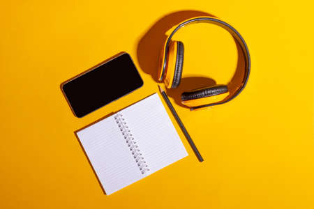 Desktop with yellow wireless headphones and an open notebook on a bright yellow backgroundの写真素材
