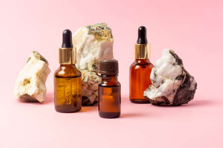 An amber bottle for essential oils and cosmetics stands next to the stone. Glass bottle on a pink background. Dropper, spray bottle. Natural cosmetics concept.の写真素材