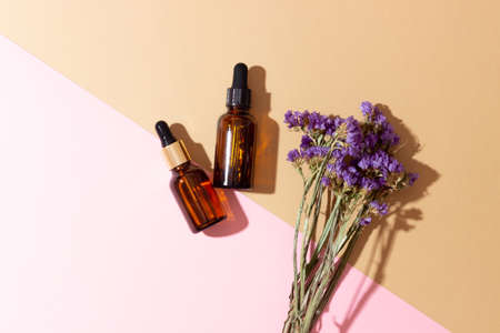 Cosmetic bottles with an eyedropper and flowers with hard shadows. The concept of using natural...