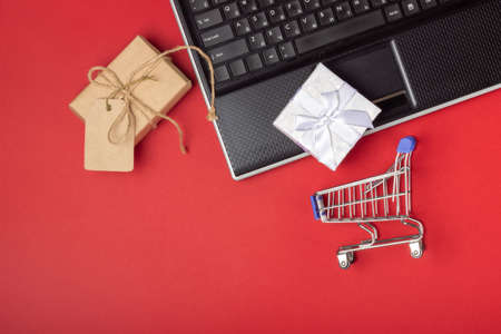Laptop, notebook, shopping cart and boxes on a bright red background. Online shopping conceptの写真素材