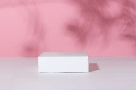 Showcase for cosmetic products. Product advertisement. Layout style design. White empty podium on a pink background with leaves and shadows. Natural cosmetics and beauty conceptの写真素材