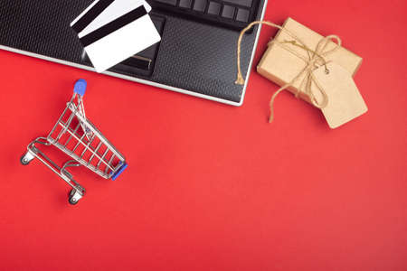 Laptop, notebook, shopping cart and boxes on a bright red background. Online shopping conceptの写真素材