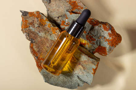 A transparent glass container with natural body and hair oil lies on the stones. Natural and bio...