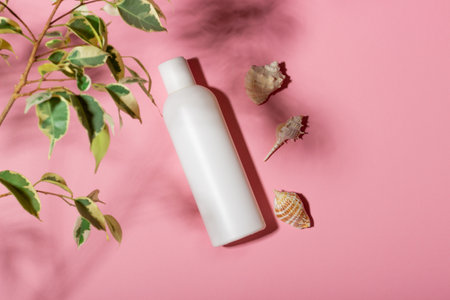 White cosmetic bottle with face cream or lotion and telana against a pink background with seashells and shadows. Sun cream, summer cosmetics.の写真素材