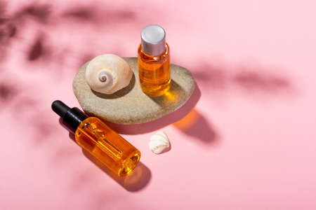 Tanning oil. Cosmetic products next to seashells in sunbeams on a pink background. Sun protective cosmetics.の写真素材