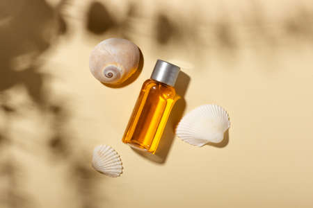 Tanning oil. Cosmetic products next to seashells in sunbeams on a pink background. Sun protective...