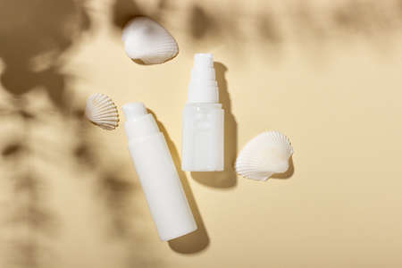 Set of white cosmetic bottles and jars with seashells on a beige background with hard shadows. The...