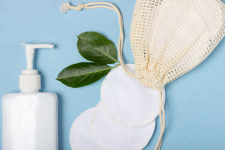 Cotton reusable make-up remover pads in a cloth bag and face wash and cleanser on a blue background. The concept of ecology and conscious consumption. Reusable cotton padsの写真素材